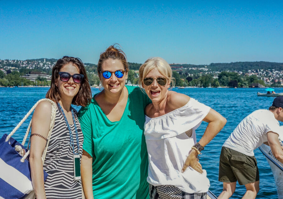 Gruppe fröhlicher Menschen beim sommerlichen Compresso-Ausflug am Zürichsee, lachend und entspannt am Wasser.