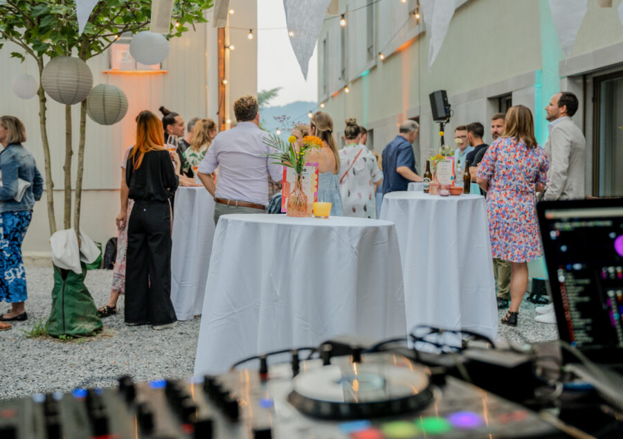 Outdoor-Networking beim Compresso Sundowner 2023: Gäste stehen mit Drinks an Stehtischen, bunte Lichter und DJ-Pult im Vordergrund.