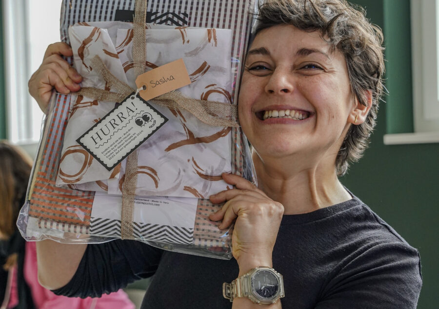 Lachende Mitarbeiterin hält stolz ein verpacktes Weihnachtsgeschenk bei Compresso in den Händen.