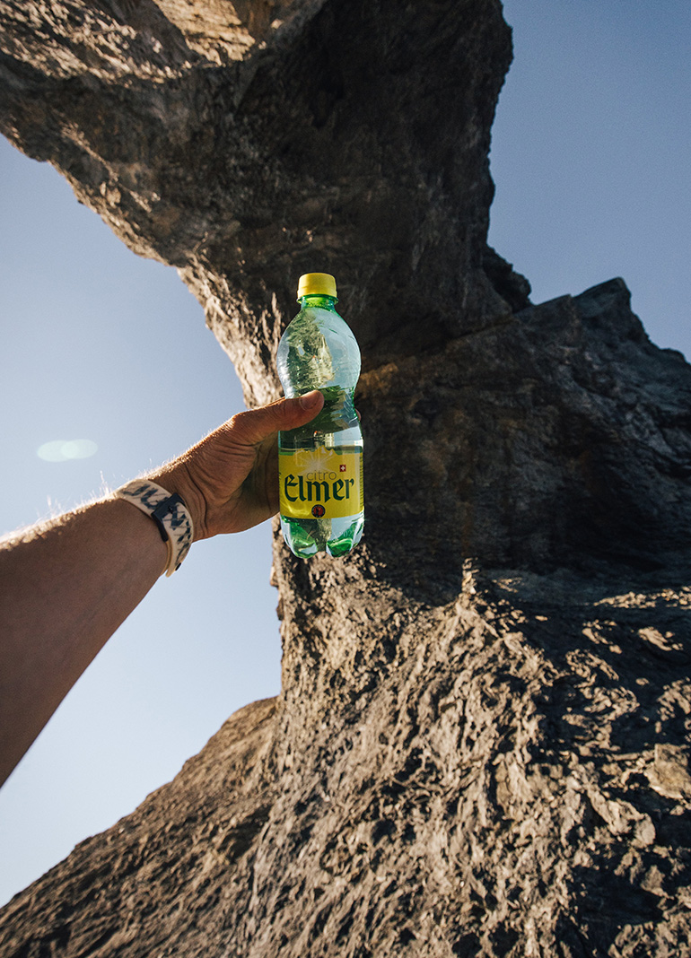 Hand hält Limonadenflasche vor Felsen