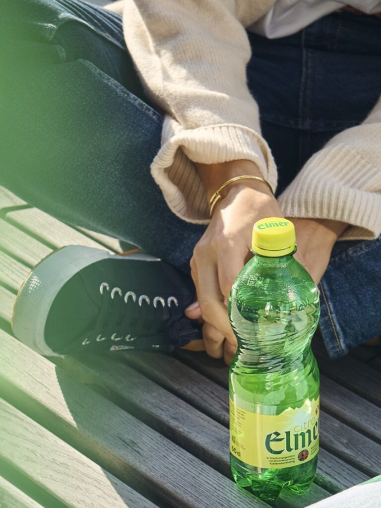 Person sitzt mit Limonadenflasche auf Holzbank
