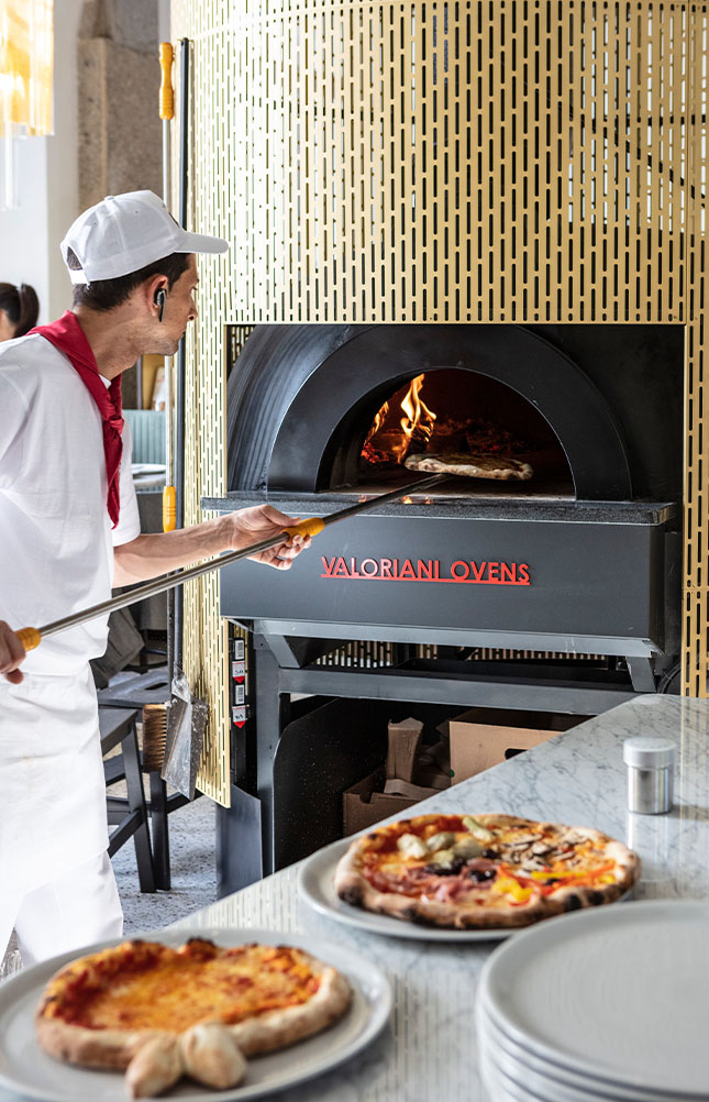 Pizzabäcker schiebt Pizza in Steinofen