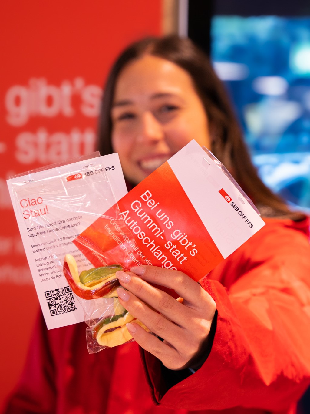 Frau mit Gummibärchen in der Hand vor SBB-Plakat