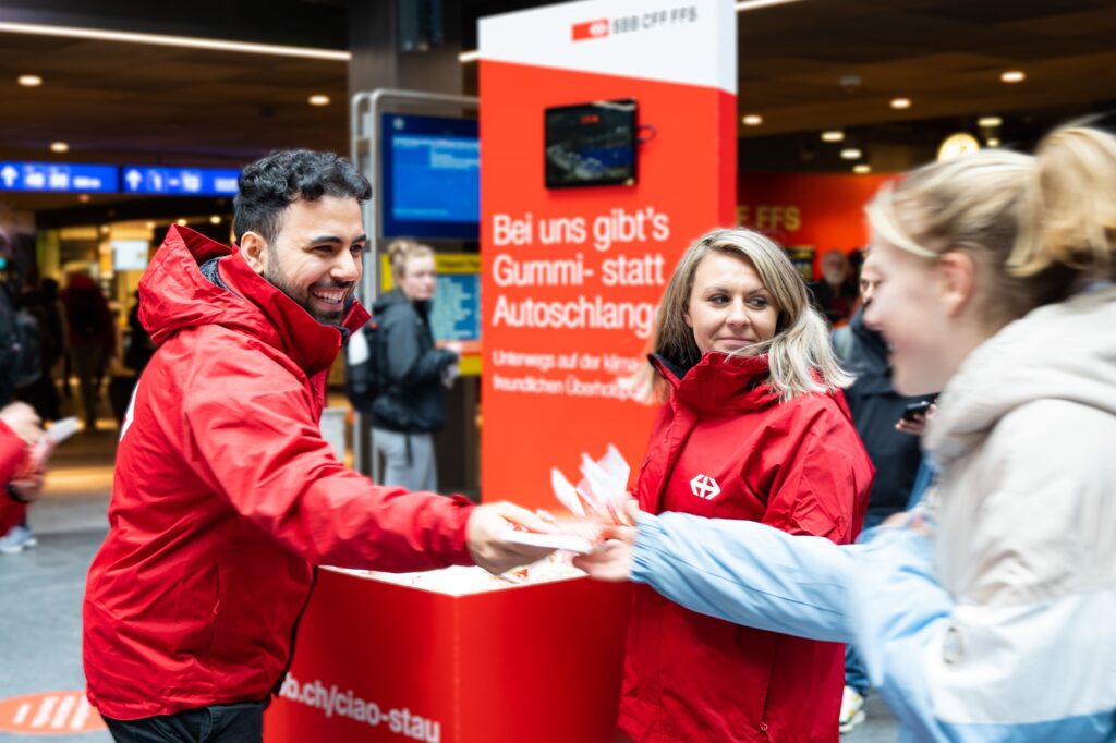 Personal in roten Jacken verteilt Flyer am Bahnhof