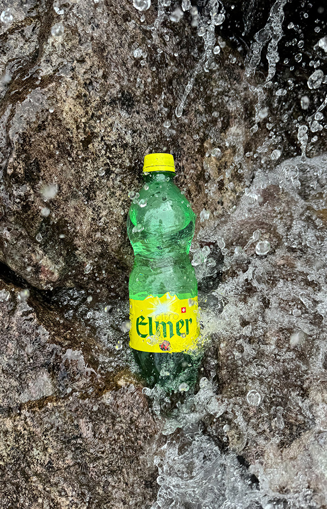 Grüne Flasche im spritzenden Wasser auf Felsen