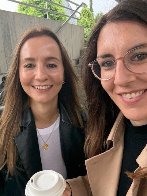 Two women smiling with coffee outdoors.
